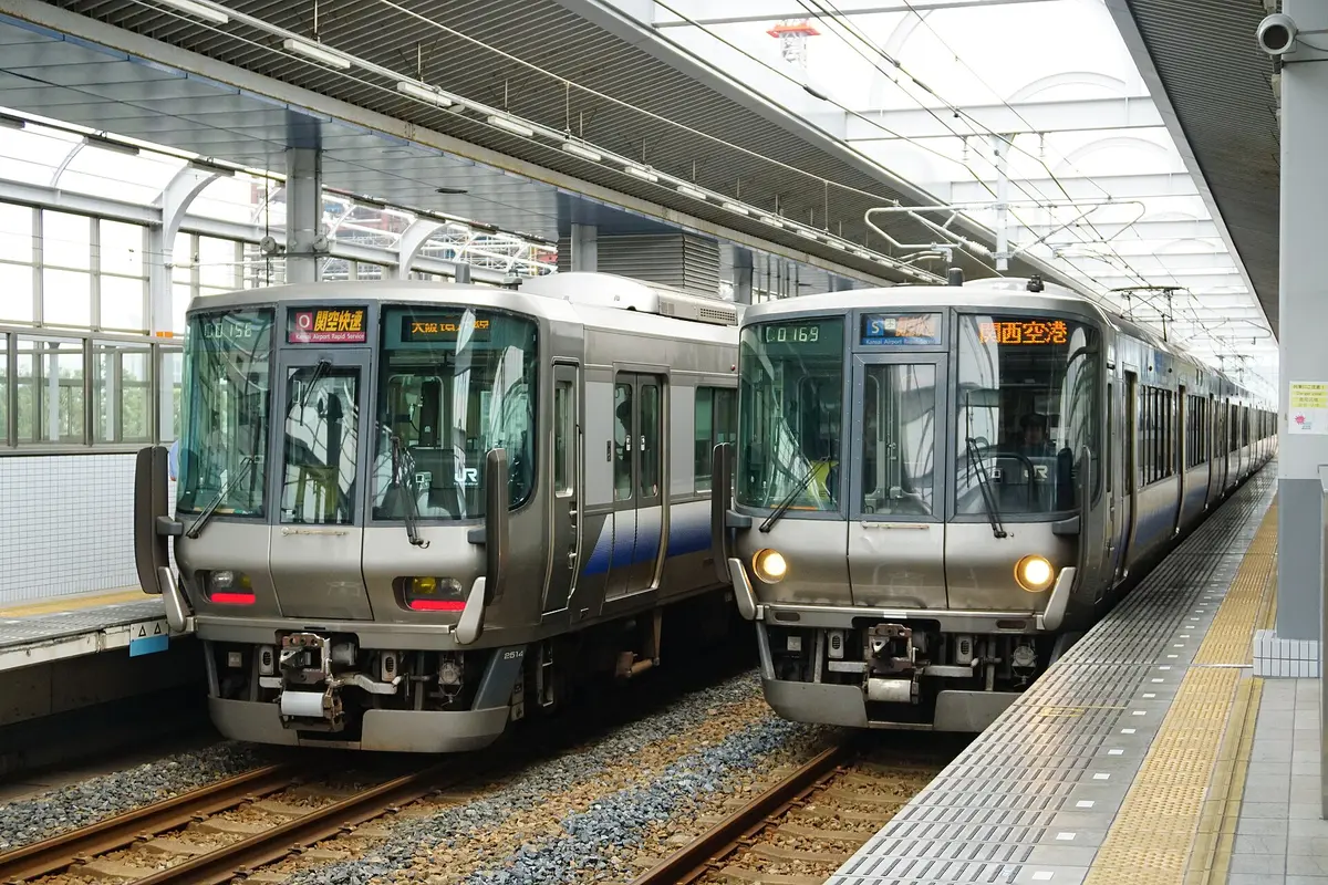 Two silver and blue JR Kansai Airport Rapid Service trains stopped on either side of a platform at Rinku Town Station